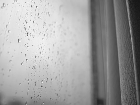 Closeup of rain drops on the window glass with curtain in the room. Black and white abstract backgroundの写真素材