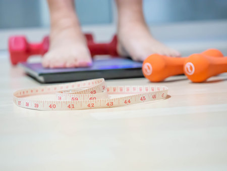 <p>Closeup of measuring tape with blurry orange, red dumbbells,&nbsp;weight scale on wooden floor and women 's foot for dieting or healthy concept</p>の写真素材
