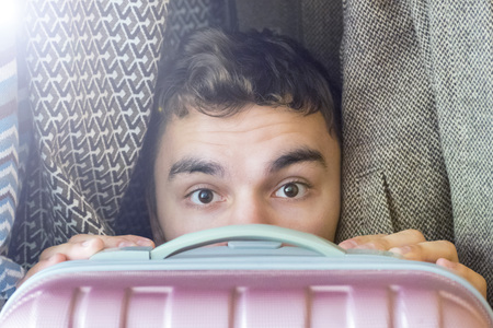 A young man hides in a closet covering yourself with a suitcaseの写真素材