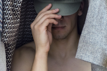 The young man covers his face with hat sitting in the closet women's clothingの写真素材