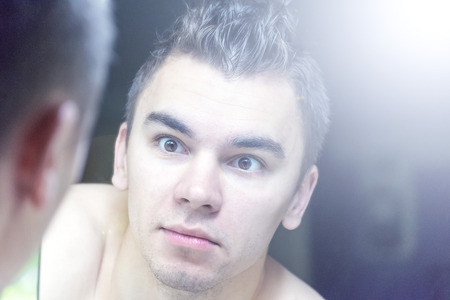 The young man looks at himself in the mirrorの写真素材