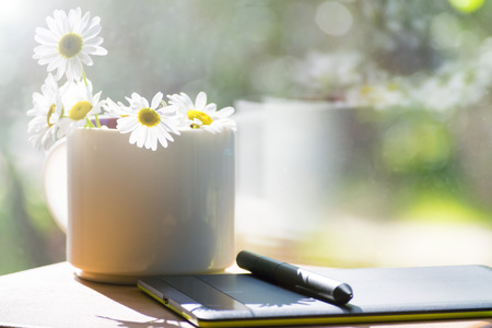 Mug, daisies, graphics tablet. The concept of am designer. A Sunny summer morning.の写真素材