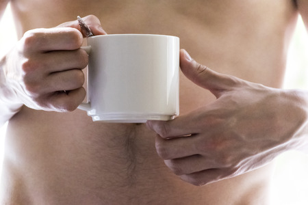 A young man holding a mug in his hands. Morning, summer, autumn, bare-chested. Tea, coffee.の写真素材