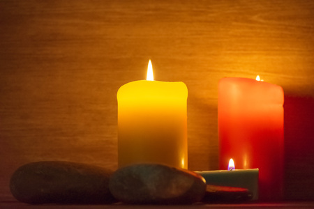 Several multi-colored candles are lit and surrounded by stones.の写真素材