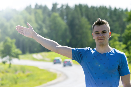 The young man catches the car on the road. Summer. Hitchhiking.の写真素材