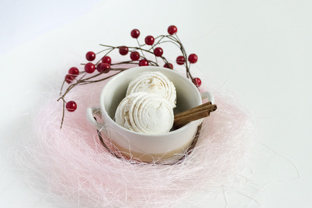 Marshmallows in a wooden plate surrounded by red berries on a light backgroundの写真素材