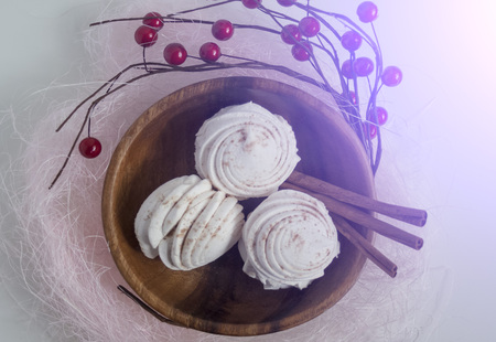 Marshmallows in a wooden plate surrounded by red berries on a light backgroundの写真素材