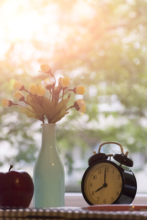 Alarm clock, notebook, vase with flowers and Apple on the desktop. The concept study.の写真素材