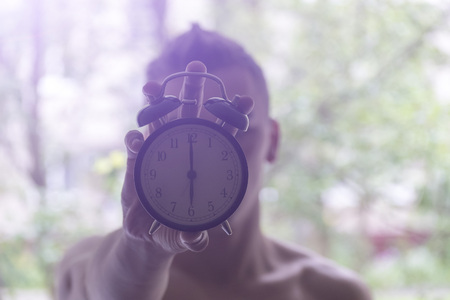 A young man holding a clock. The concept of active in the morning. Awakening.の写真素材