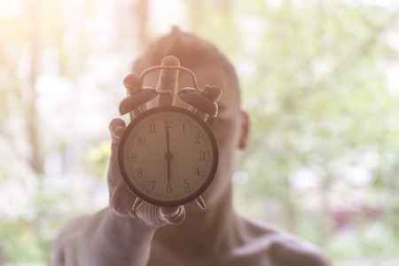 A young man holding a clock. The concept of active in the morning. Awakening.の写真素材