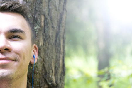 A young man sits under a tree and listens to musicの写真素材