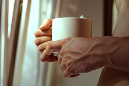 A young man holding a mug in his hands. Morning, summer, autumn, bare-chested. Tea, coffee.の写真素材