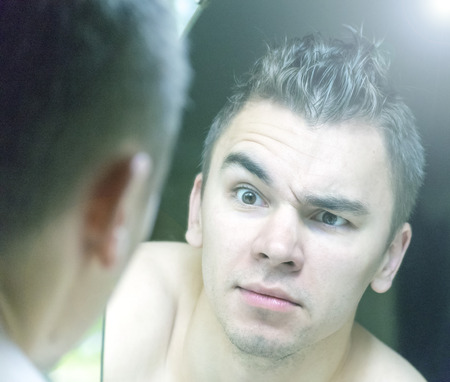 The young man looks at himself in the mirrorの写真素材