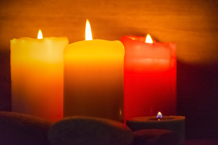Several multi-colored candles are lit and surrounded by stones.の写真素材
