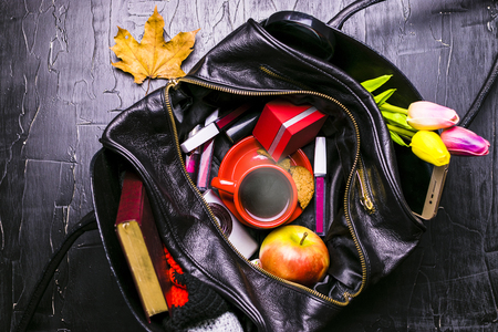 The contents of the female handbag. Flowers, lipstick, camera, coffee, biscuits, beads. Dark background.の写真素材