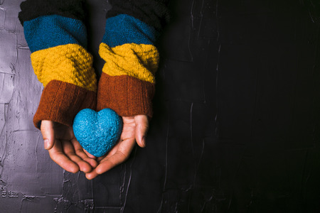 Male hand holds out a blue heart on black backgroundの写真素材