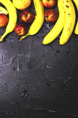 Apples and bananas on a dark background with splashes of waterの写真素材