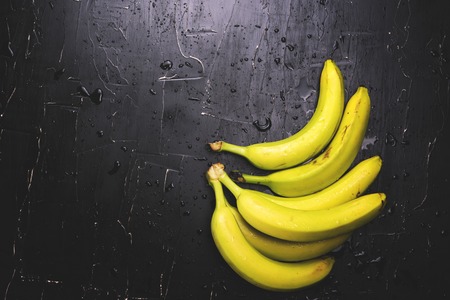 Apples and bananas on a dark background with splashes of waterの写真素材