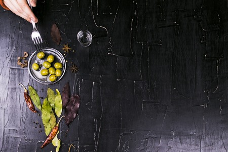 Man bites olives alcoholic beverage surrounded by spices. Dark textured background.の写真素材