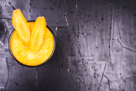 Fresh carrot juice in glass on dark textured backgroundの写真素材