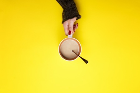 Girl holding a mug of coffee on a yellow background. The concept of a pause, a break.の写真素材
