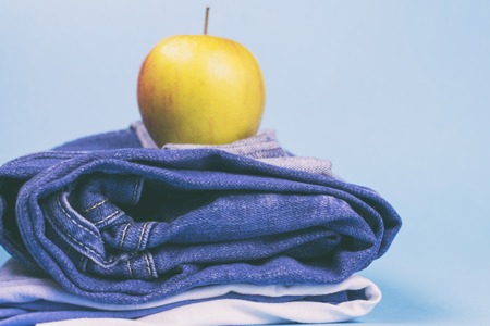 Women's jeans folded in a pile, and on top of the Apple, on a colored background. Made in a vintage performance.の写真素材