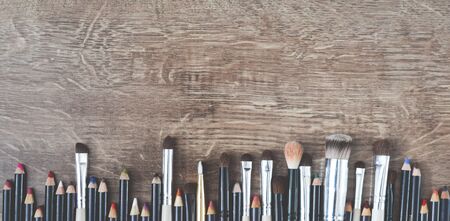 Cosmetic brushes and pencils lie on a wooden brown floor