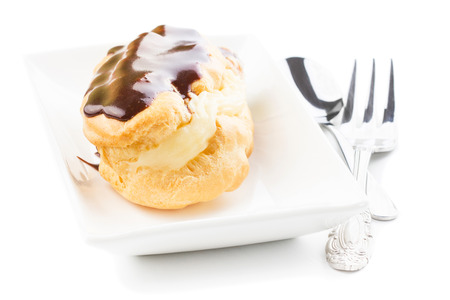 Chocolate eclair on a white plate with an elegant fork, isolated on white