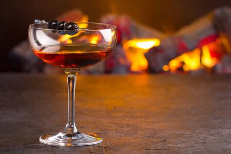 A glass of classic Manhattan cocktail on fireplace background