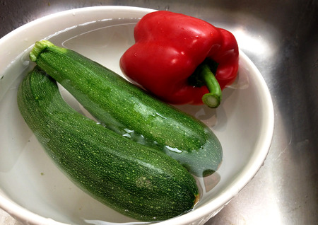 Fresh zucchini and red bell pepper in a bowl with water.の写真素材