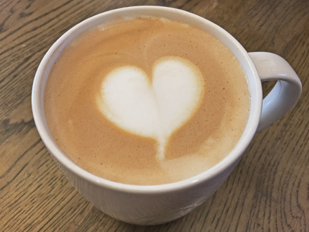 Coffee latte with milk foam designed as heart shape art on wooden table.の写真素材