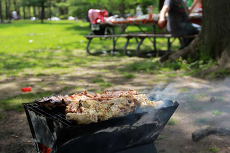 Barbeque grill with smoking meat and picnic table at the background の写真素材