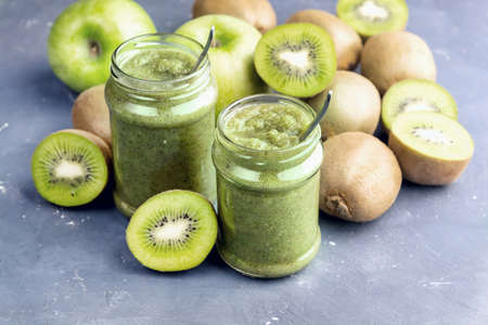 Two jars with green smoothie Kiwi and apple around jarsの写真素材