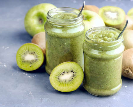 Two jars with green smoothie Kiwi and apple around jarsの写真素材