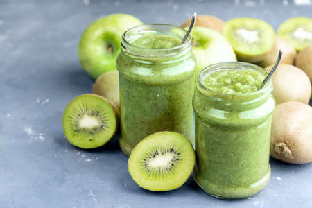 Two jars with green smoothie Kiwi and apple around jarsの写真素材