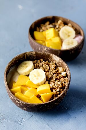 Granola With Yogurt Banana and Mango Tasty Healthy or Diet Breakfast Vertical Coconut Bowls Blue Backgroundの写真素材
