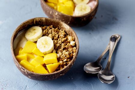 Tasty and Healthy Breakfast in Coconut Bowls Granola With Yogurt Banana and Mango Top View Horizontal Copy Spaceの写真素材
