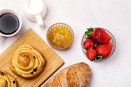 Tasty Breakfast Freshly Baked Buns with Raisins and Cinnamon Cup of Black Coffee Cream Ripe Strawberry and Orange Jam in Glass Bowl Top View Copy Spaceの写真素材