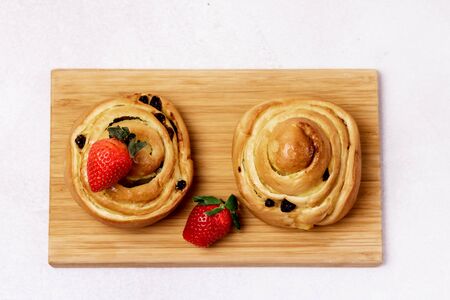 Freshly Baked Buns with Raisins and Cinnamon Decorated with Strawberry on Wooden Tray Light Gray Background Top View Sweet Homemade Pastry Swedish Dessertの写真素材