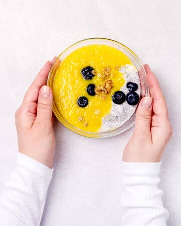 Female Hand are Holding Glass Bowl with Healthy Food Bowls of Muesl and Yogurt with Berry and Mango Top Viewの写真素材