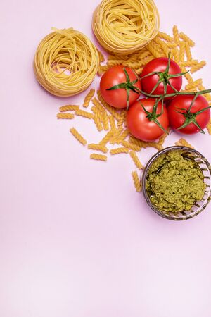 Dry Raw PastaTagliatelle Pesto Parmesan Cheese Raw Tomato Top View Pink Background Top View Verticalの写真素材