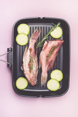 Fresh Sea Bass with Raw Zucchini on Black Grill Pan Pink Background Raw Fish and Vegetable Ready for Cooking Healthy Dinner Top Viewの写真素材
