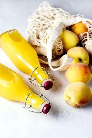 Natural Peach Juice in a Bottle and Eco Bag with Ripe Peaches Gray Background Healthy Diet Drink Verticalの写真素材