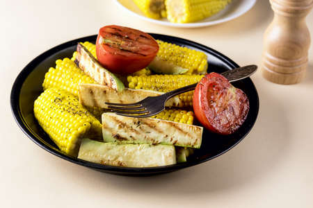 Black Plate of Grilled Vegetable Zucchini, Corn, Tomato Tasty and Healthy Diet Food Yellow Backgroundの写真素材