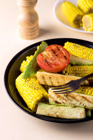 Black Plate of Grilled Vegetable Zucchini, Corn, Tomato Tasty and Healthy Diet Food Yellow Background Verticalの写真素材