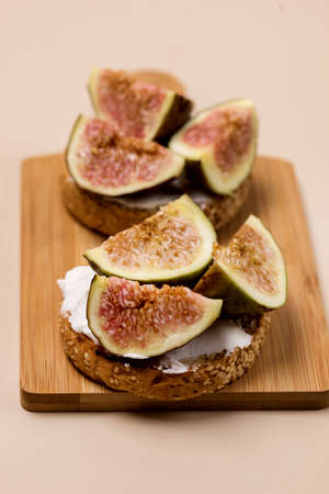 Tasty Canape or Crostini Toasted Baguette Cream Cheese and Figs on Wooden Board Delicious Appetizer Lunch Yellow Background Verticalの写真素材