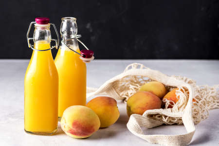 Natural Peach Juice in a Bottle and Eco Bag with Ripe Peaches Gray Background Healthy Diet Drink Horizontalの写真素材