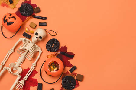Halloween Background Halloween Sweets and Candy Small Jack-O-Lantern Pumpkin Basket with Candy Autumn Leaves Skeleton Orange Background Top View Copy Spaceの写真素材