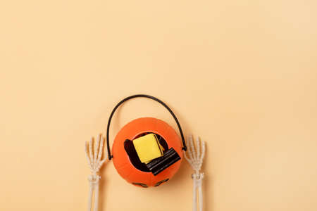 Skeleton Arms Holding Small Jack-O-Lantern Pumpkin Basket with Candy Yellow Background Top View Copy Spaceの写真素材