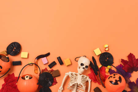 Halloween Background Halloween Sweets and Candy Small Jack-O-Lantern Pumpkin Basket with Candy Autumn Leaves Skeleton Orange Background Top View Copy Spaceの写真素材